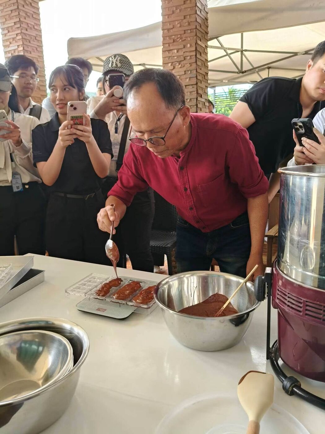 The farmer pouring chocolate into moulds while students watch and take photos